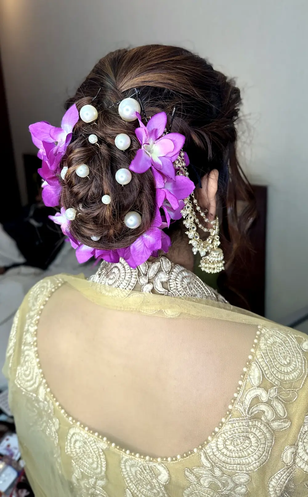 Back view of a client's braided bun styled with purple orchids and pearl pins, a jhumka earring, and an embroidered sheer blouse back