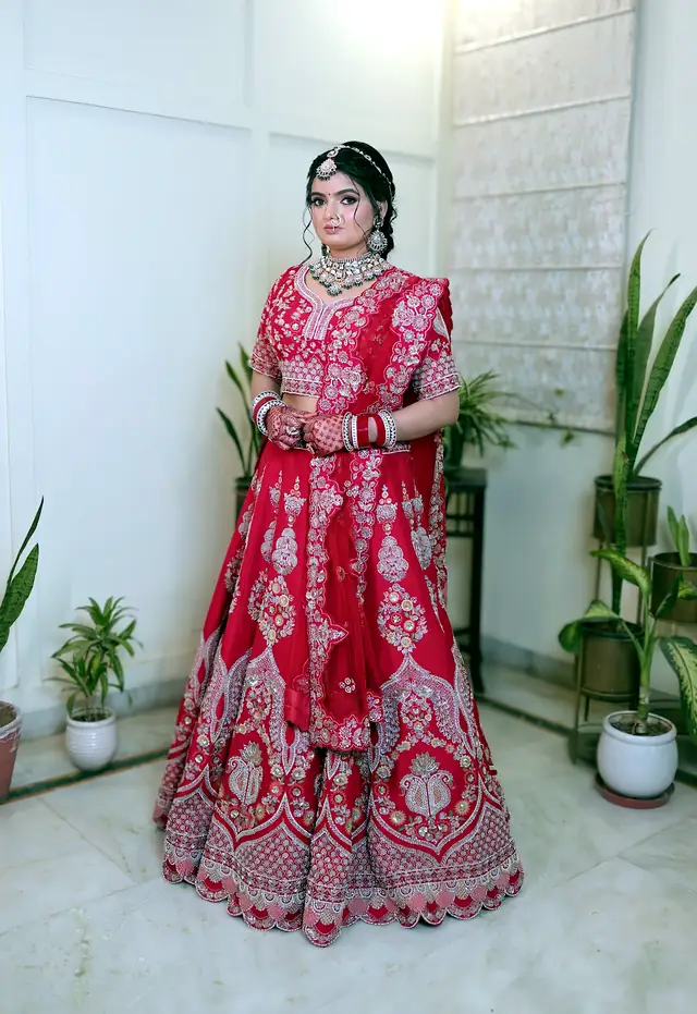 Bride in a red bridal lehenga with emerald-toned jewellery, photographed on a rooftop at golden hour