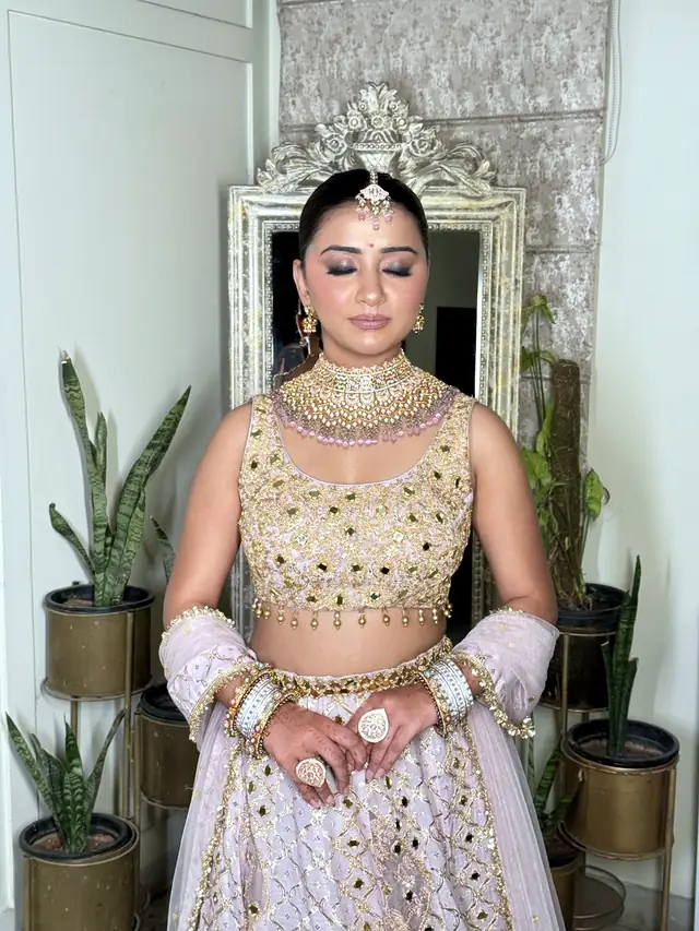 Bride in a pale lilac lehenga with mirror-work embroidery, standing in front of an ornate mirror frame