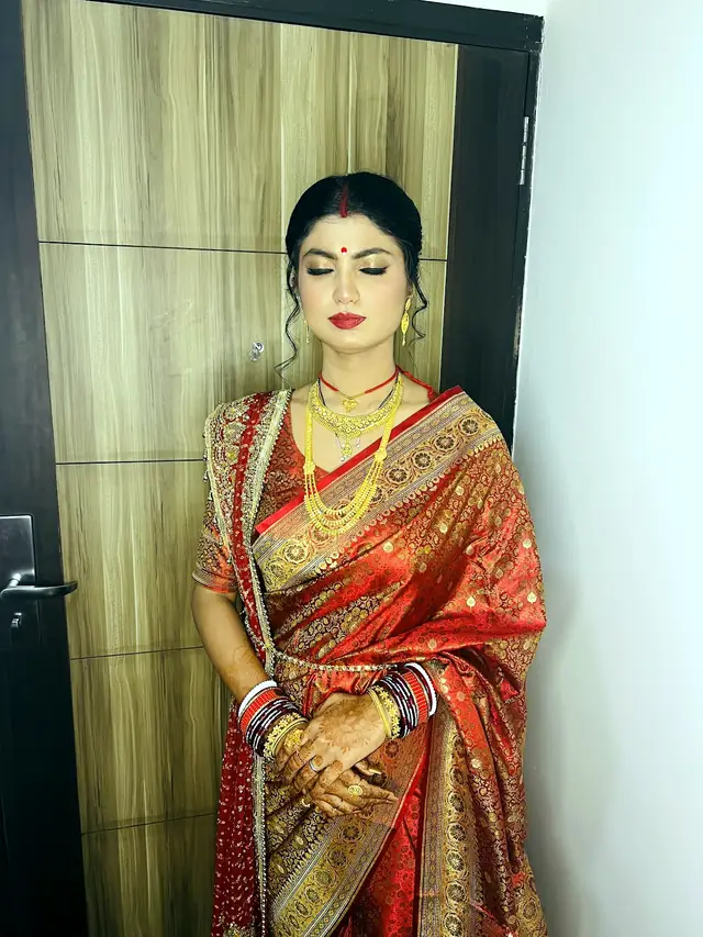 Bride in a red and gold saree with layered gold necklaces and red and white bangles